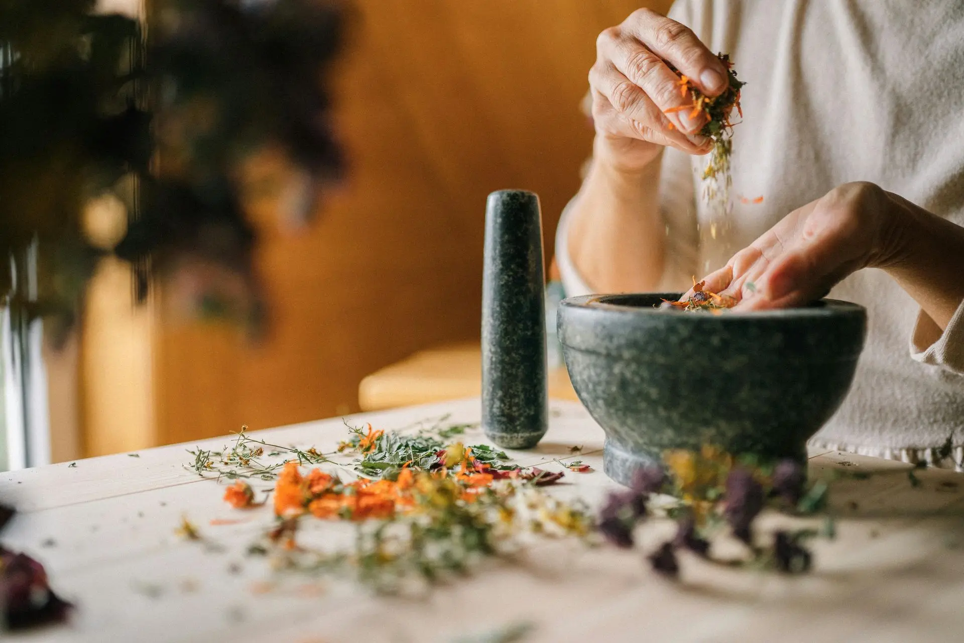 Fresh botanicals, grounded by tradition Hands mixing dried flowers in a stone mortar.